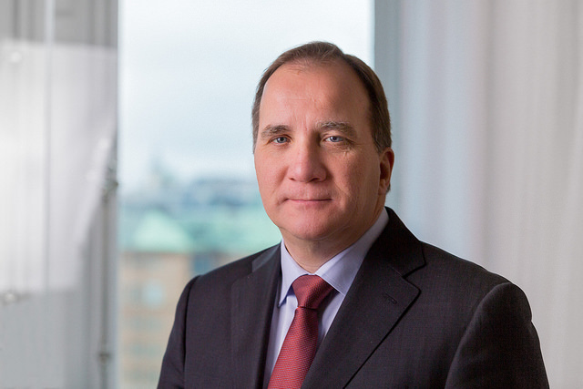 Stefan Löfven sitter i ett rum. Han har kavaj och slips på sig. Han har tunt, kort brunt hår och ganska buskiga ögonbryn. Han har stor näsa och små ögon. Han tittar in i kameran och ser ganska allvarlig ut.