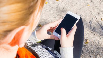 Bild på person snett uppifrån som håller i en smartphone. Man kan inte se ansiktet på personen.