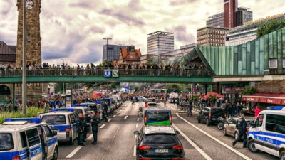 Väg i Hamburg med många polisbilar. Längre bort på vägen är det många människor som protesterar.