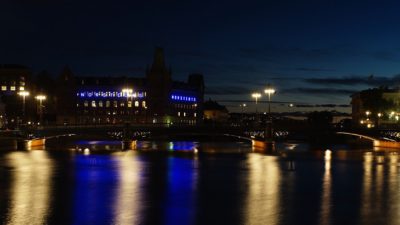 Några hus syns på andra sidan en sjö. På husen lyser det lampor, och det är mörkt på himlen.