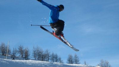 En skidåkare i blå jacka hoppar med sina skidor och armarna utsträckta
