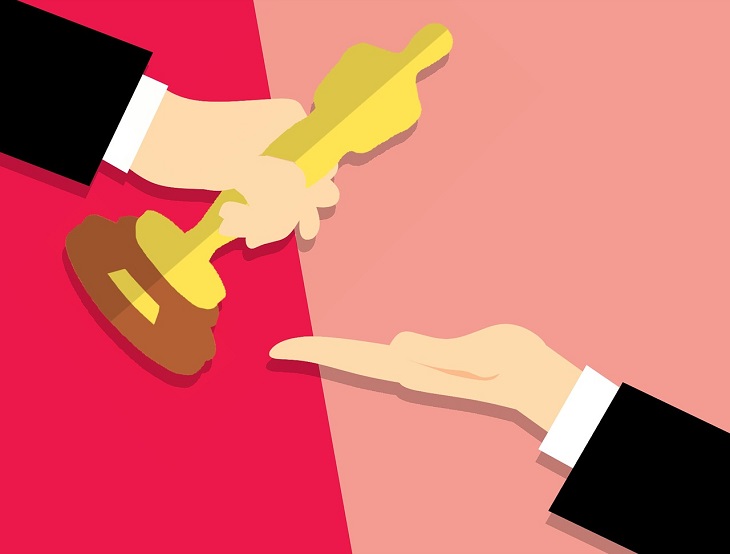 En tecknad bild på två armar med svarta kostymer. Den ena handen ger en oscarsstatyett till den andra handen. Statyetten är formad som en gubbe och är gjord av guld.