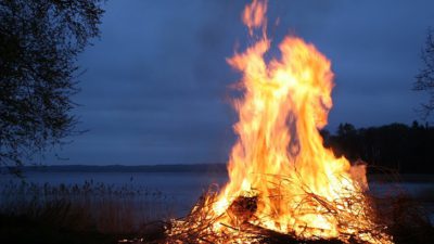 En stor brasa brinner i mörker, vid en sjö.