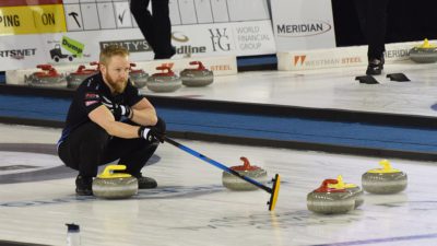 Bild på Niklas Edin under en match. Han står hukad på isen och pekar var hans medspelare ska träffa curlingstenen för att slå bort motståndarna.