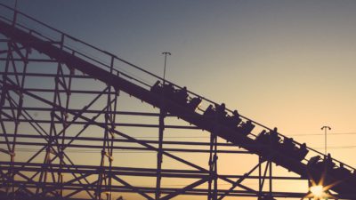 Bild på en berg- och dalbana där vagnarna är påväg upp för en lutning. Det är mystiskt ljus på himlen och solen håller på att gå ner.